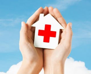 Hands holding a cutout of a house with a red cross